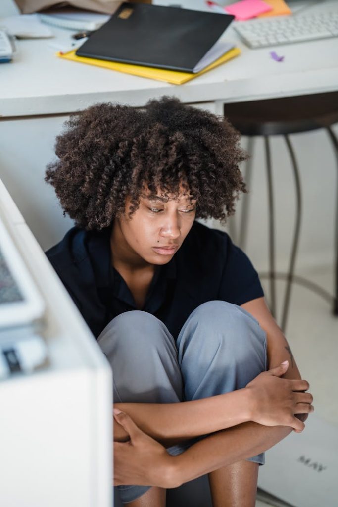 African American woman showing stress and depression under an office desk.